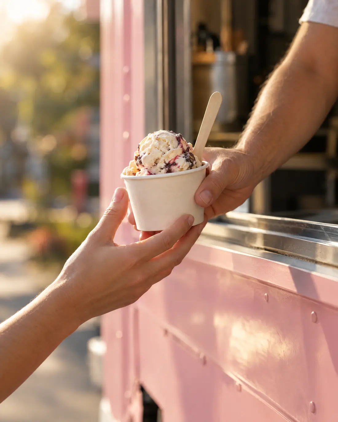 Eine Hand reicht einen Becher Eis aus dem Fenster des Foodtrucks